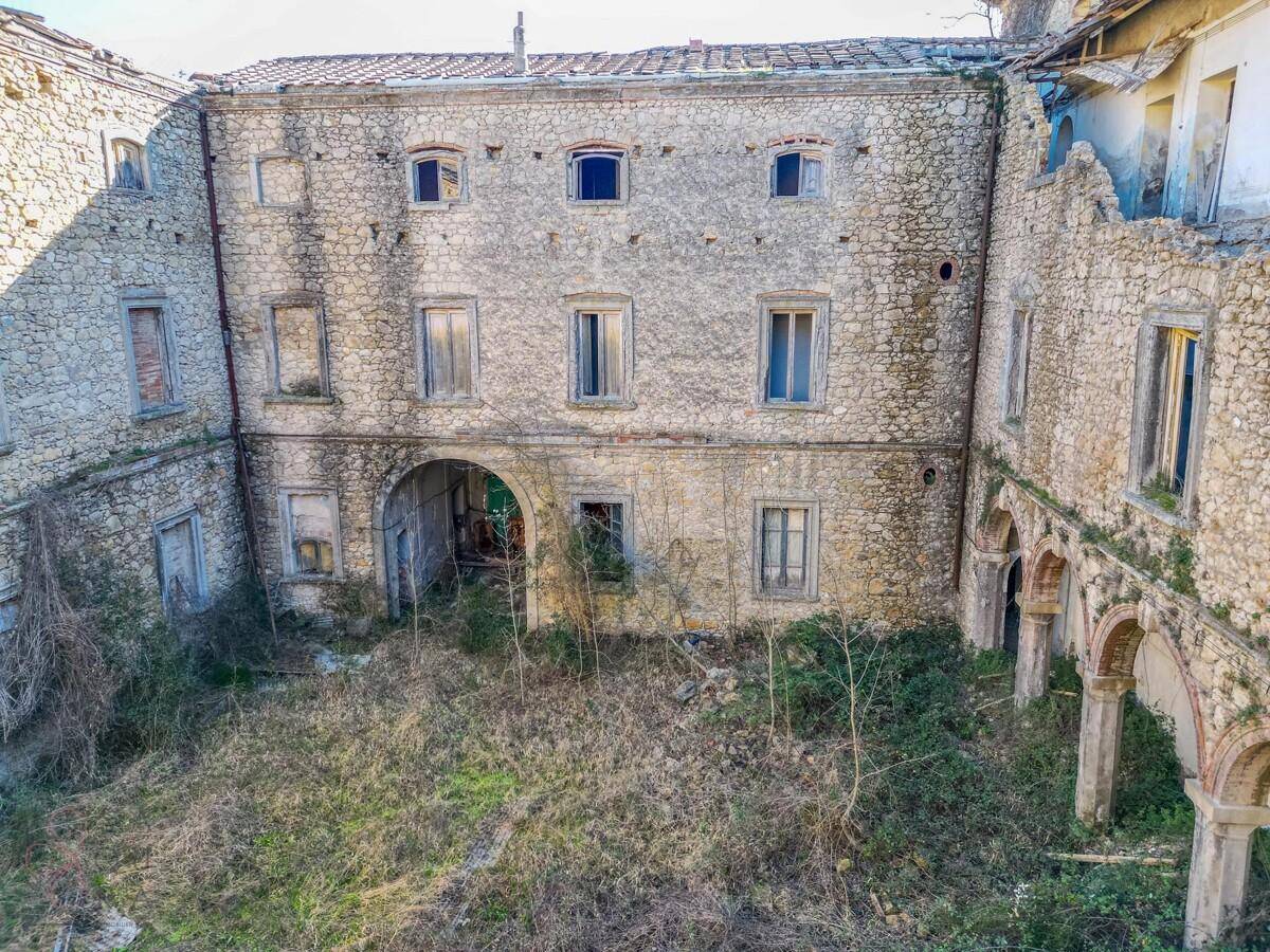 Überwachsener Innenhof eines historischen Anwesens mit verfallenen Mauern und Bögen.