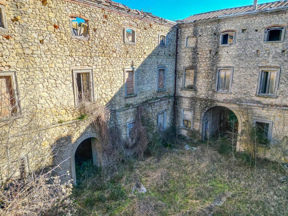 Historischer Innenhof mit verfallenen Arkaden und starker Vegetation, unter blauem Himmel.