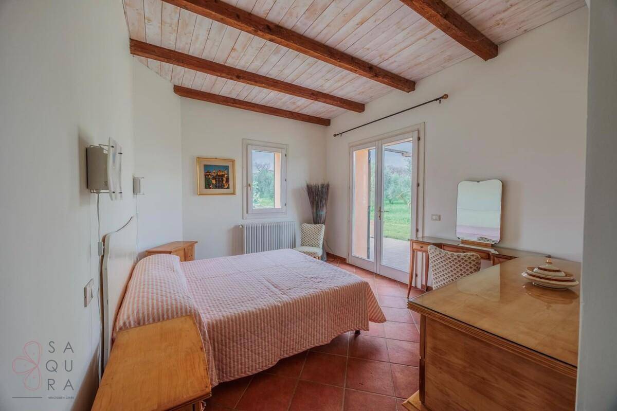 Schlafzimmer mit Holzbalkendecke, Doppelbett und Zugang zum Außenbereich.