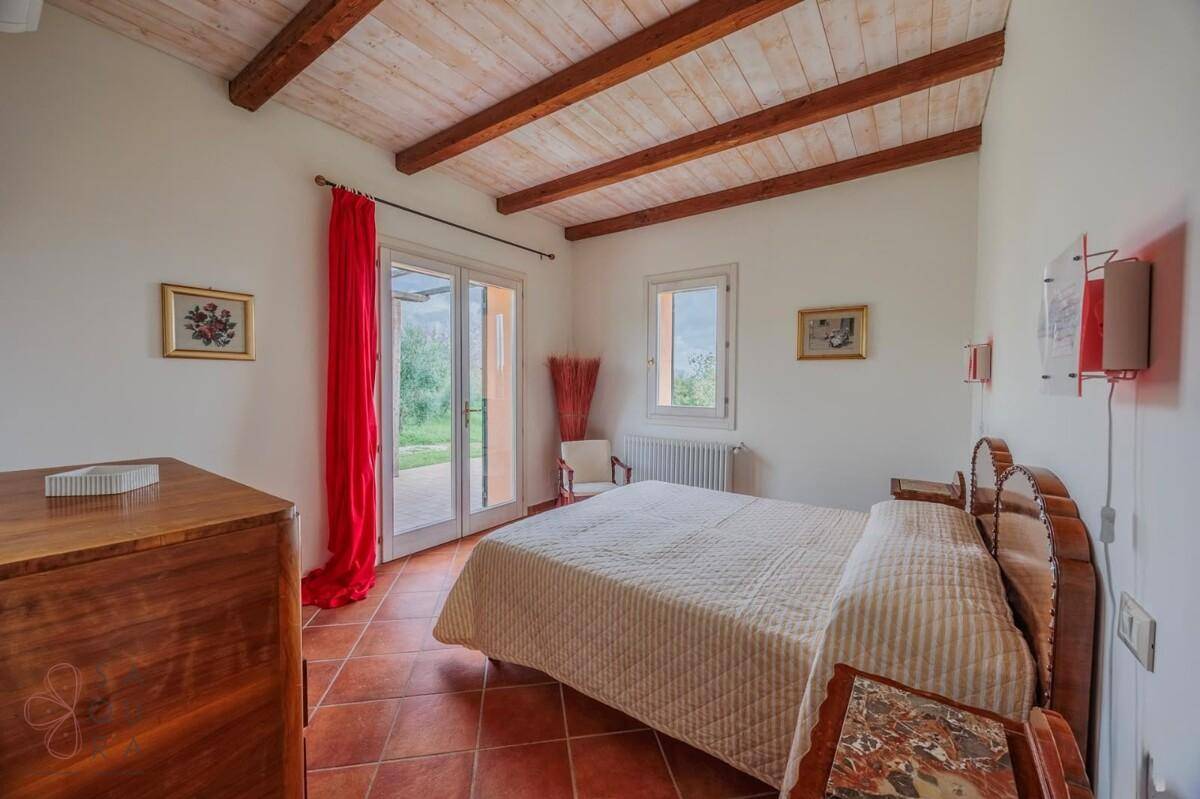 Helles Schlafzimmer mit Holzbalkendecke, Doppelbett und Zugang zur Terrasse.
