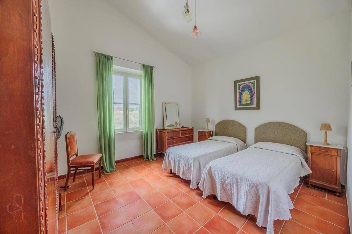 Schlafzimmer mit zwei Einzelbetten, Terrakottafliesen und grünen Vorhängen.