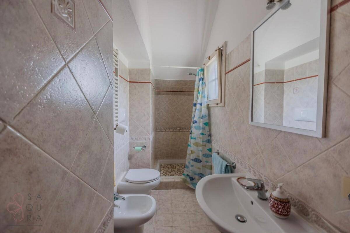 Badezimmer mit beigefarbenen Fliesen, Duschbereich, WC, Bidet und Spiegel.