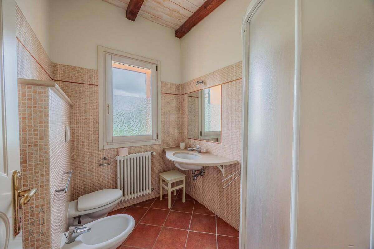 Badezimmer mit Terrakottafliesen, Duschkabine, WC, Bidet und Fenster.