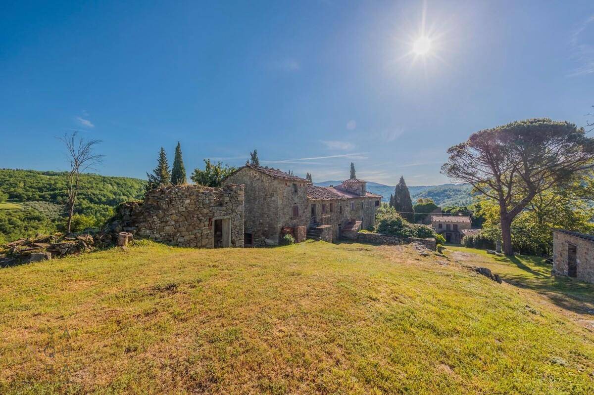 Historisches Anwesen aus Stein in hügeliger Landschaft unter strahlend blauem Himmel mit viel Sonne.