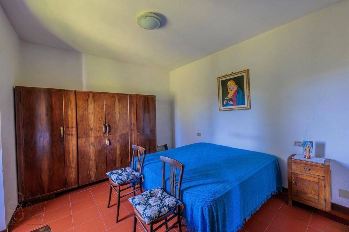 Schlafzimmer mit Terrakottaboden, Holzschrank und einem blauen Bettüberwurf in schlichter Einrichtung.