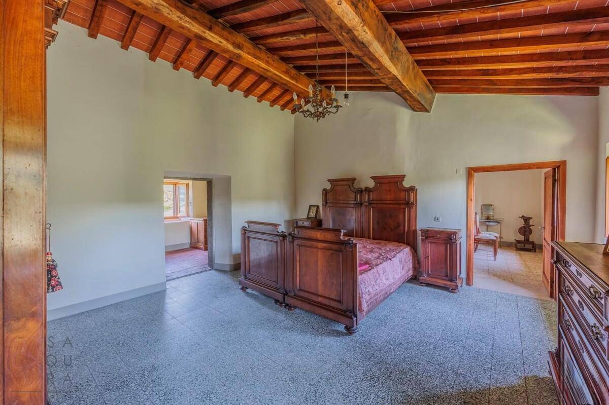 Großes Schlafzimmer mit Holzbalkendecke, Terrazzoboden und antiken Holzmöbeln.
