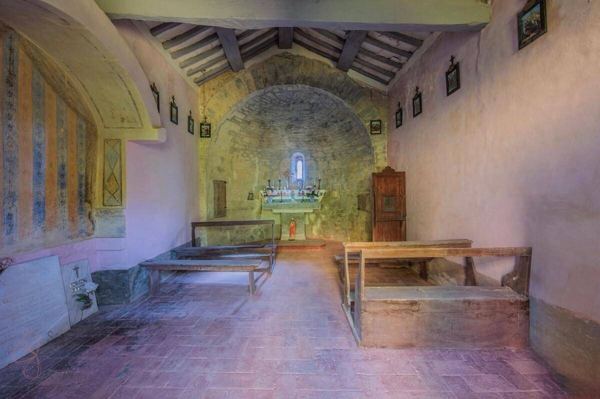 Historische Kapelle mit Steinaltar, Holzbänken und sichtbaren Holzbalken in einem alten Gebäude.