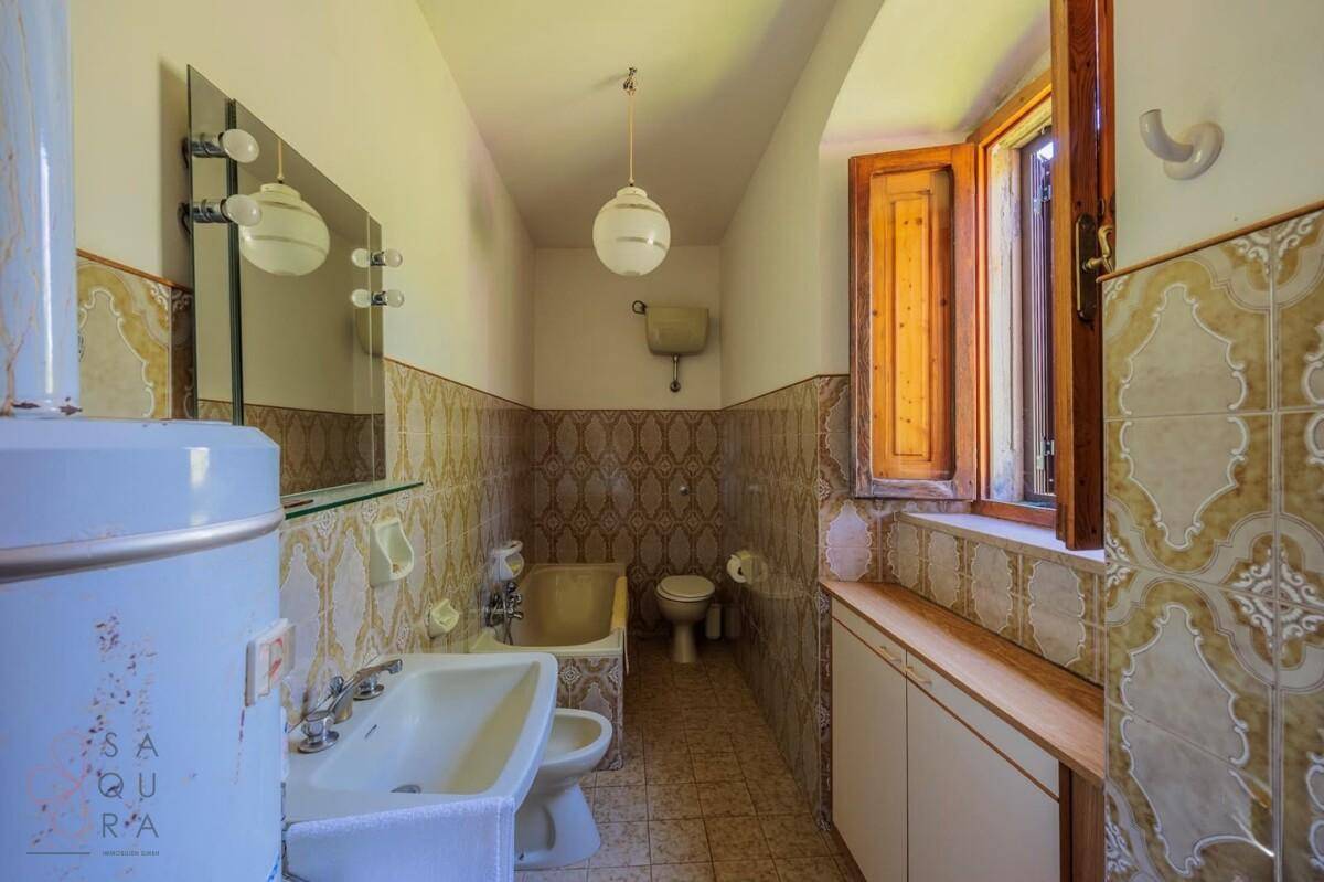 Badezimmer im 80er-Jahre-Stil mit gemusterten Fliesen, Fenster und einfacher Ausstattung.