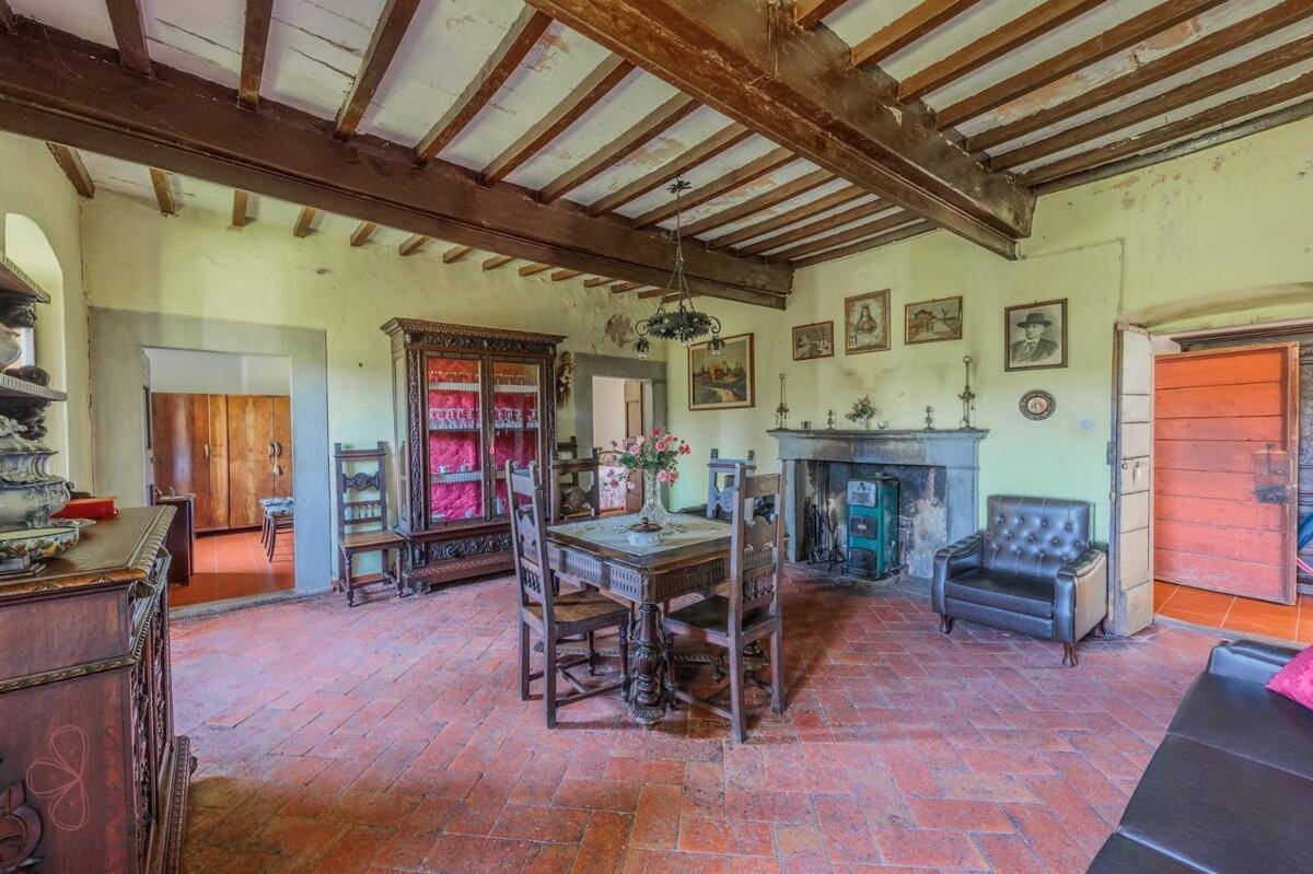 Geräumiges Wohnzimmer mit Holzbalkendecke, Kamin und Terrakottaboden, eingerichtet im traditionellen Stil.