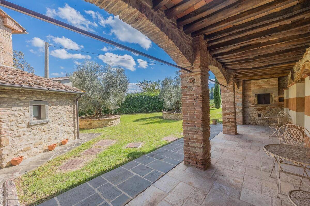 Gemütlicher Sitzbereich unter der Loggia mit rustikalen Möbeln und Blick auf den grünen Garten.