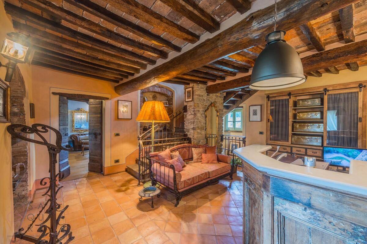 Gemütlicher Wohnraum mit sichtbaren Holzbalken, Terrakottafliesen und einer eleganten Treppe.