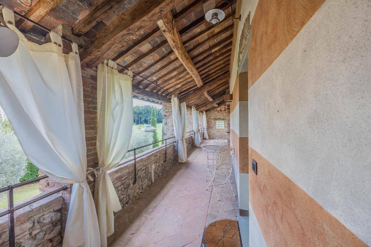 Überdachter Balkon mit rustikalen Holzbalken, Steinmauer und weitem Blick in die Landschaft.