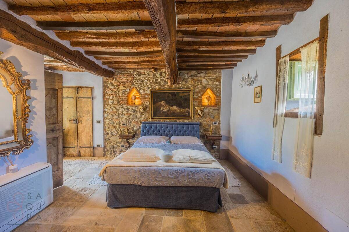 Schlafzimmer mit Holzbalken, Steinwand und großem Bett.