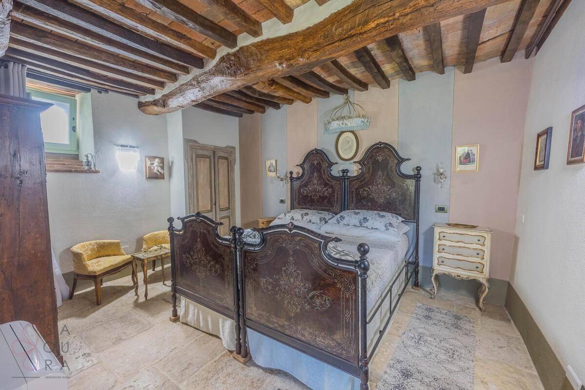 Schlafzimmer mit Holzbalkendecke, Steinfliesen und antikem Doppelbett.