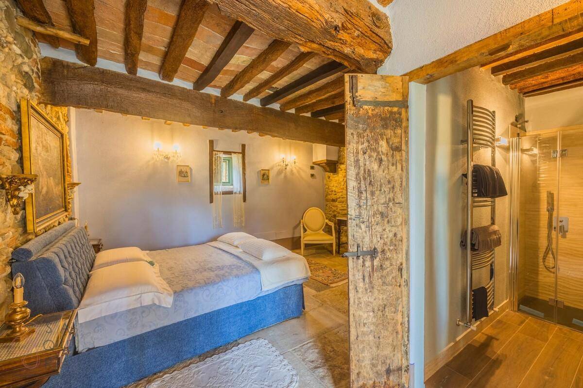 Schlafzimmer mit Holzbalken, Steinfliesen und angrenzendem Duschbad.