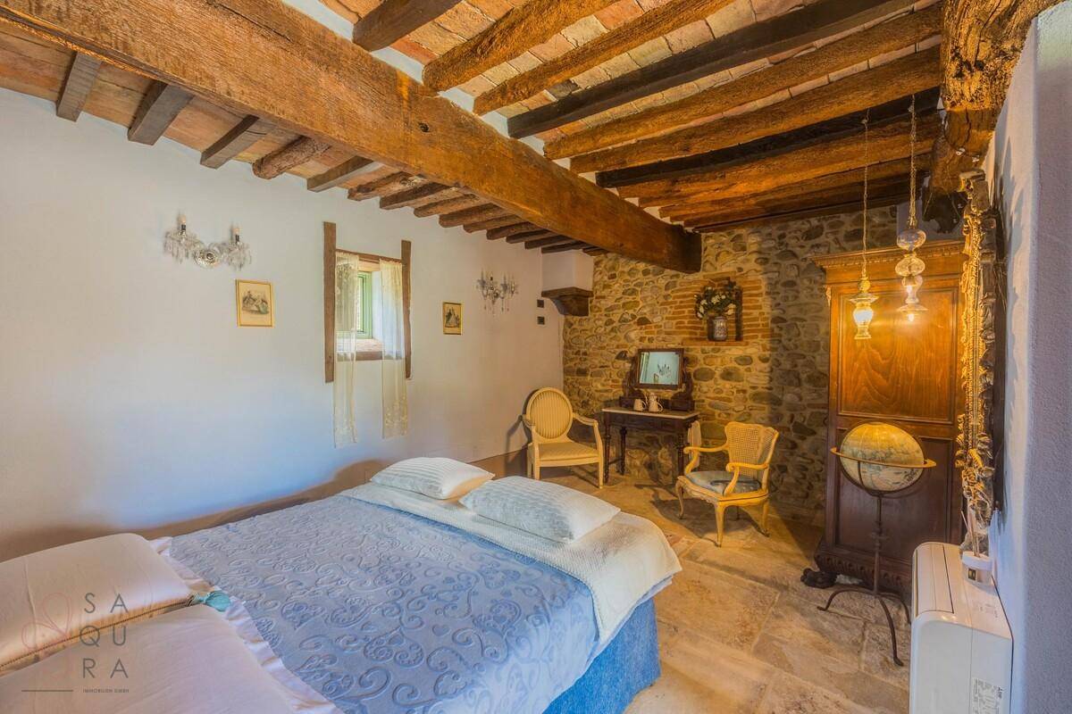 Schlafzimmer mit Holzbalkendecke, Steinfliesen und rustikaler Steinwand.