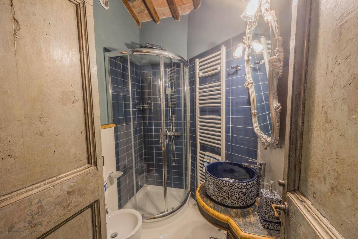 Badezimmer mit blauen Fliesen, Dusche, Bidet und dekorativem Waschbecken.