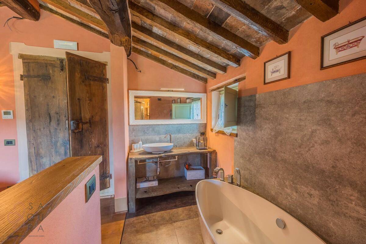Geräumiges Badezimmer mit Badewanne, Holzwaschtisch und Terrakottaboden.