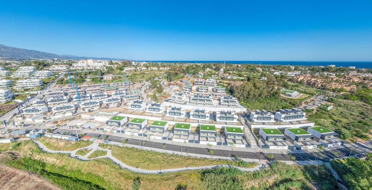 Luftaufnahme einer neuen Wohnanlage mit modernen Häusern, grünen Dächern und weitem Blick auf das Meer.