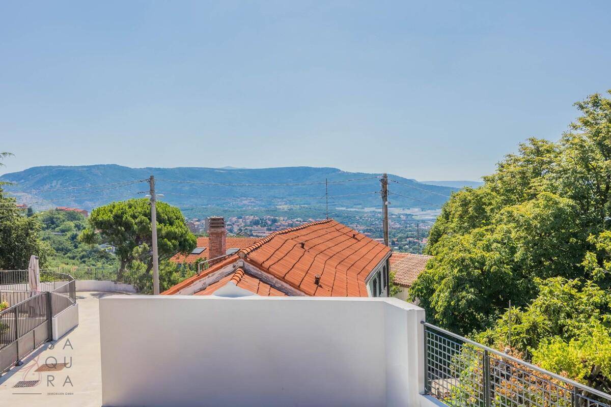 Weitläufiger Panoramablick über die Landschaft mit Bergen und Dächern in der Ferne.