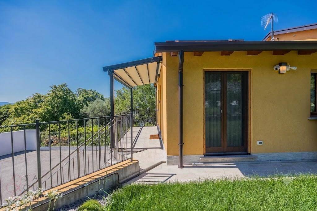Überdachte Terrasse mit Pergola und Zugang zum Haus, umgeben von Grünflächen und Weitblick.
