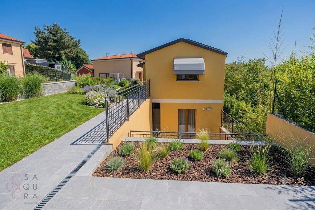Hausfassade mit modern gestalteter Gartenanlage und Treppenabgang unter blauem Himmel.