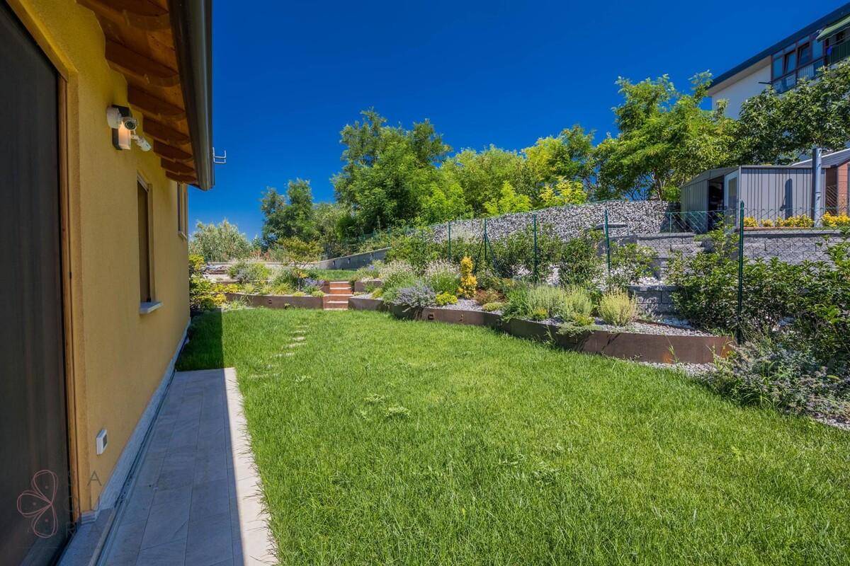 Langer, gepflegter Rasenbereich neben dem Haus mit terrassierten Beeten und üppiger Vegetation.