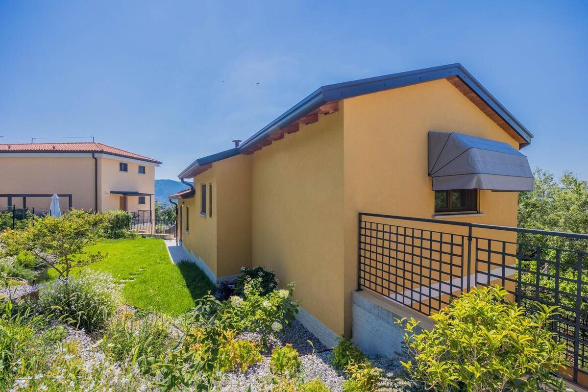 Gelbe Hausfassade mit Terrassenbereich und gepflegtem Garten unter blauem Himmel.