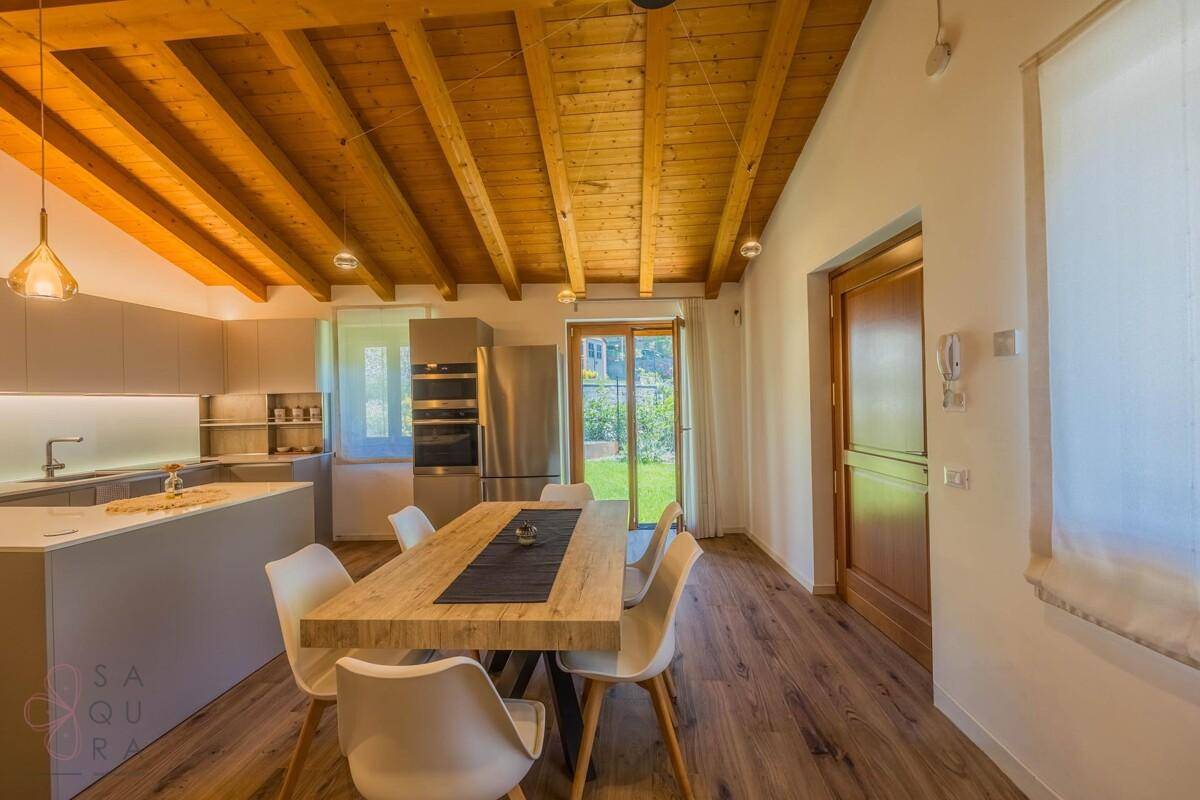 Helle Küche und Essbereich mit Holzbalkendecke, modernen Geräten und Zugang zum Garten.