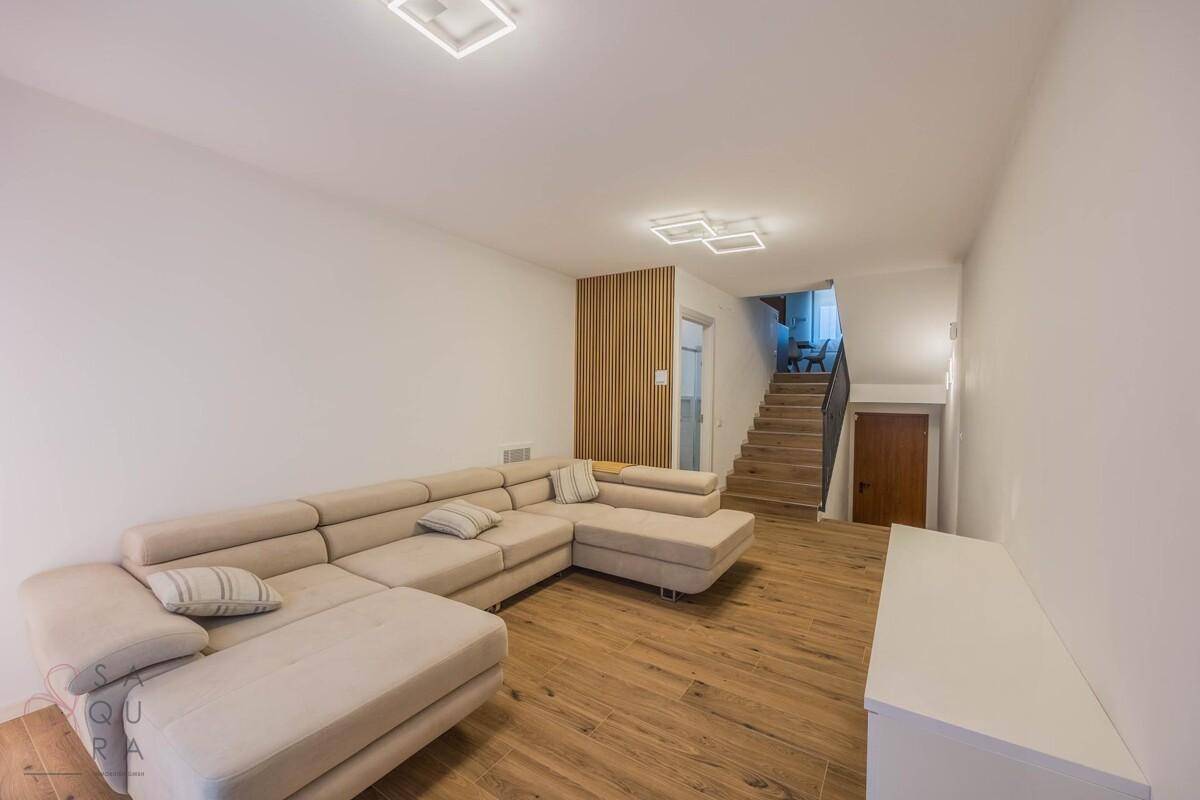 Geräumiges Wohnzimmer mit beigem Ecksofa, Holzfußboden und Treppenaufgang.