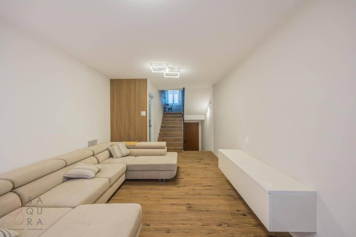 Modernes Wohnzimmer mit langem Sofa, schwebendem TV-Möbel und Holzfußboden.