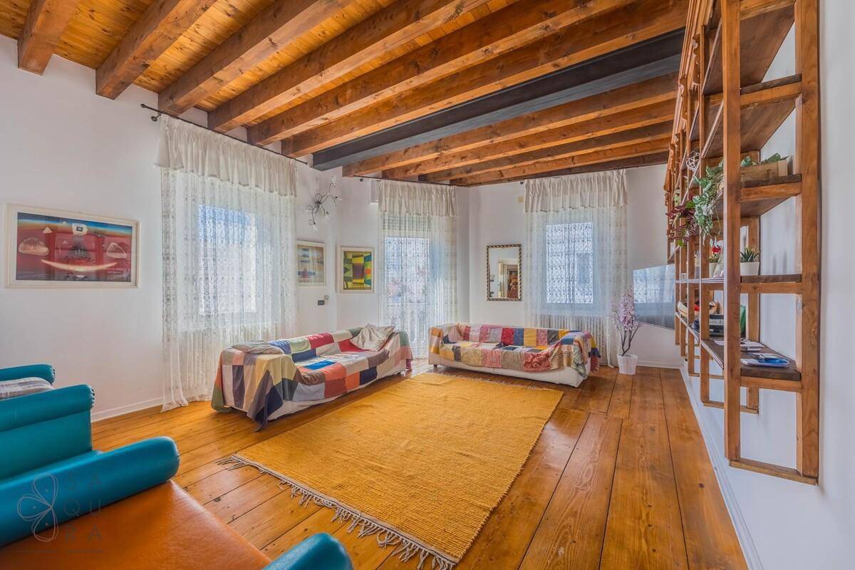 Gemütliches Wohnzimmer mit sichtbaren Holzbalken, Dielenboden und farbenfrohen Sofas.