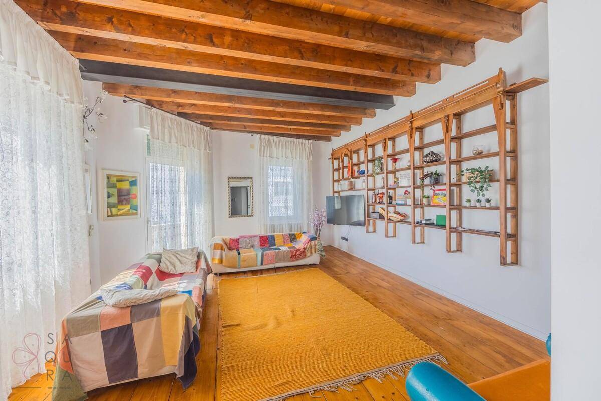 Helles Wohnzimmer mit Holzbalkendecke, Dielenboden und einer großen Bücherwand.
