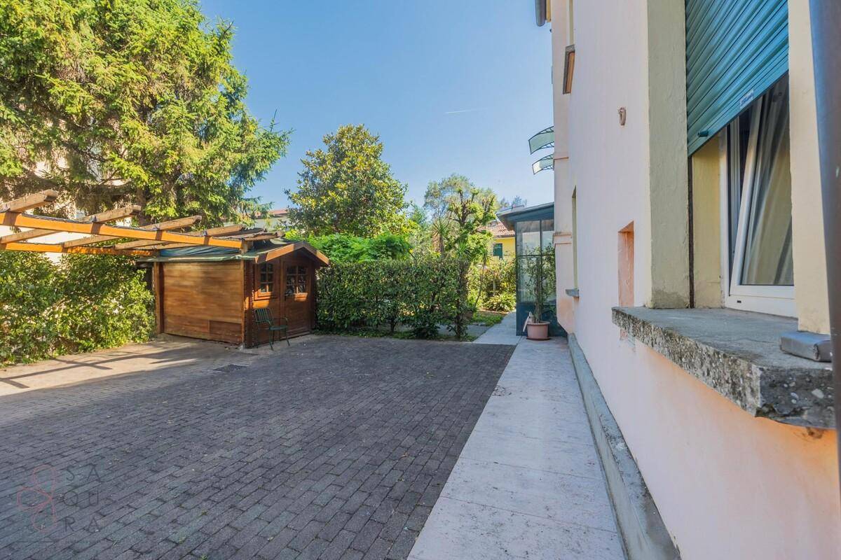 Gepflasterter Hofbereich mit Holzschuppen und einer Pergola, umgeben von hohen Bäumen.