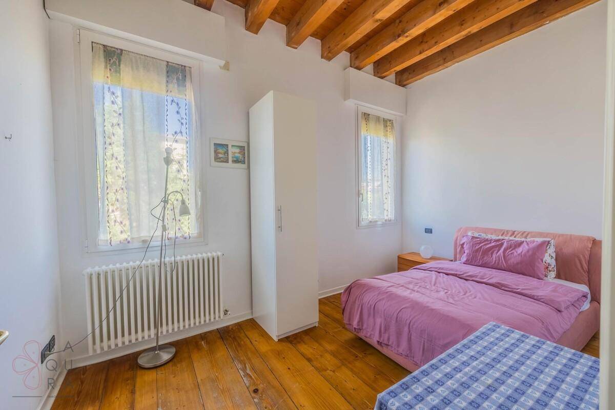 Helles Schlafzimmer mit Bett, Heizkörper unter dem Fenster und Dielenboden.