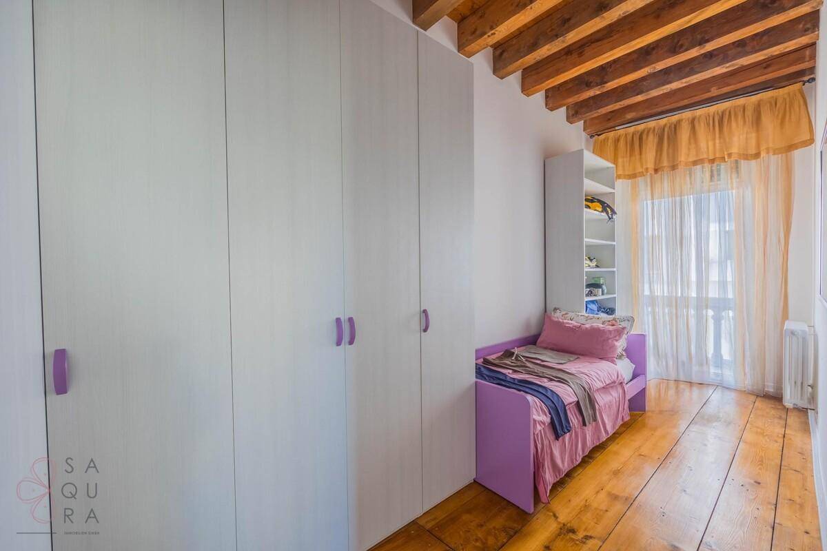Kinderzimmer mit Einzelbett, Einbauschränken und sichtbaren Holzbalken an der Decke.