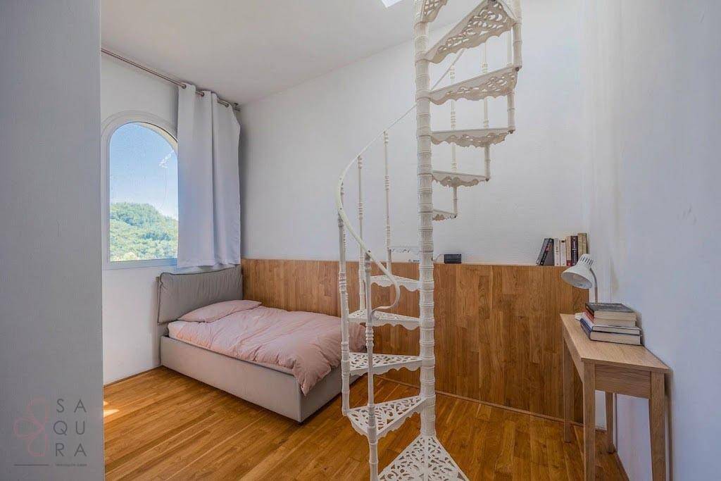 Helles Schlafzimmer mit Holzboden, Einzelbett, Holzvertäfelung und einer Wendeltreppe.
