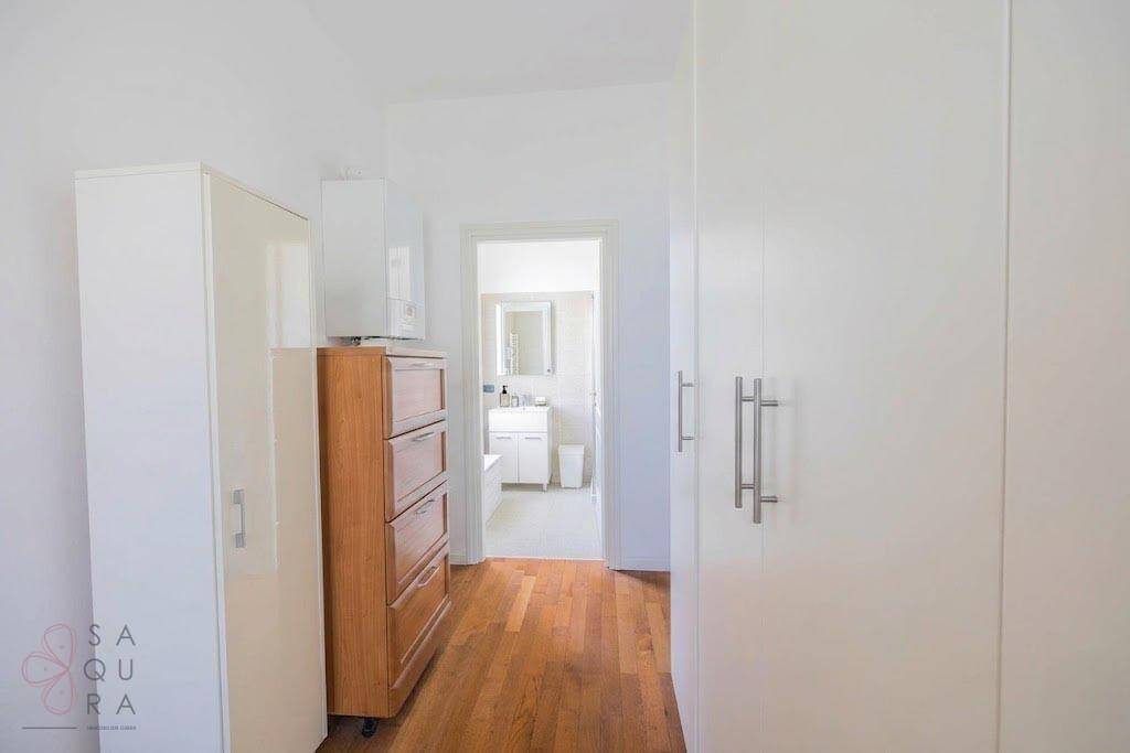 Flur mit Holzboden und Schränken, der zu einem hellen Badezimmer führt.