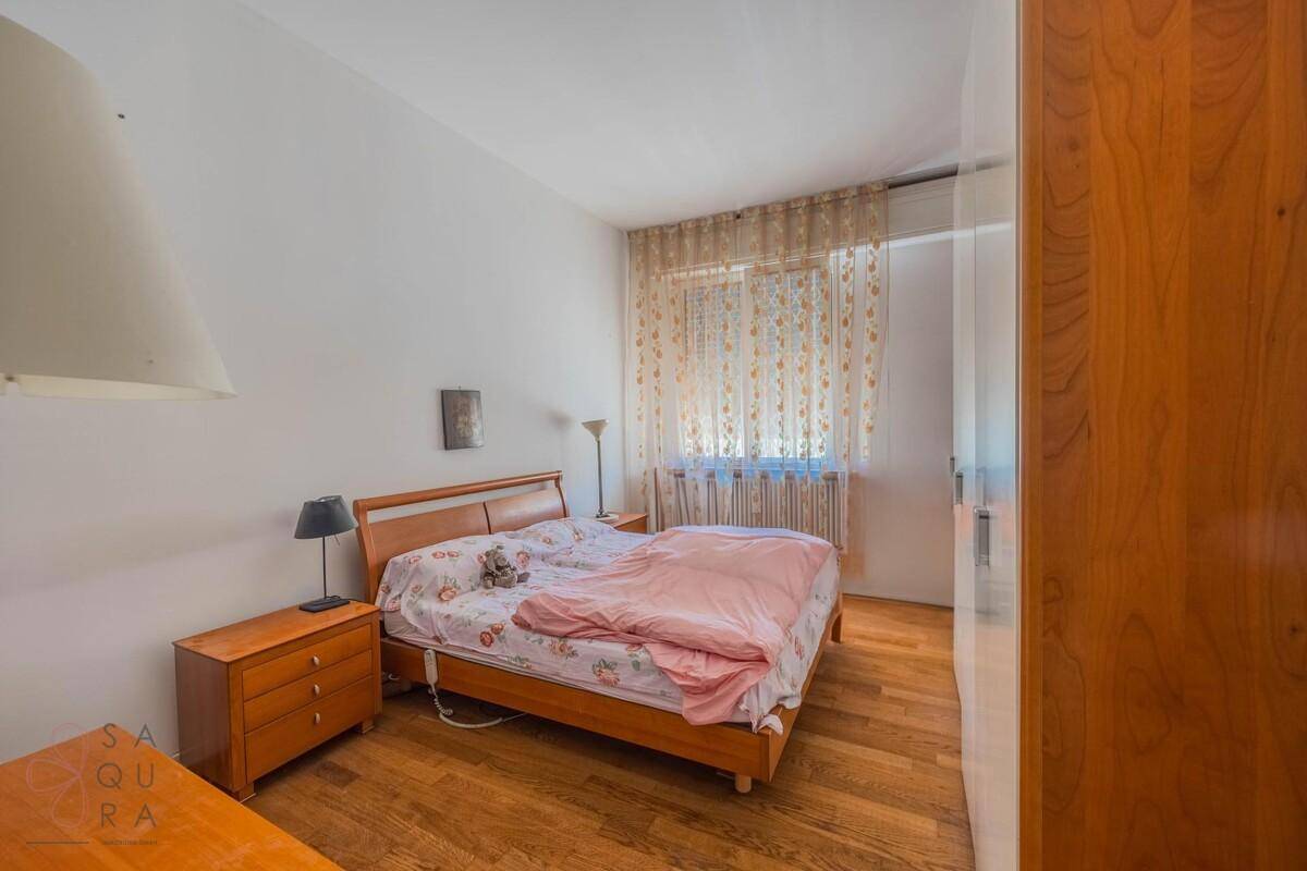 Helles Schlafzimmer mit Holzboden, Doppelbett und großem Fenster mit Vorhängen.