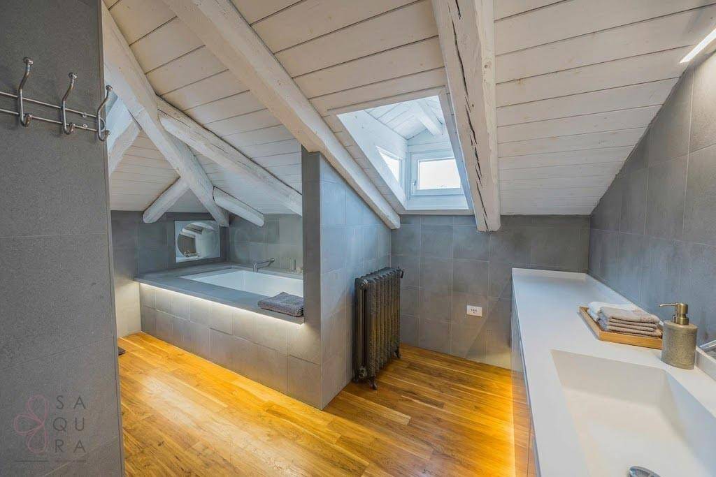Modernes Dachgeschossbad mit grauen Fliesen, Badewanne und Dachfenster für natürliches Licht.