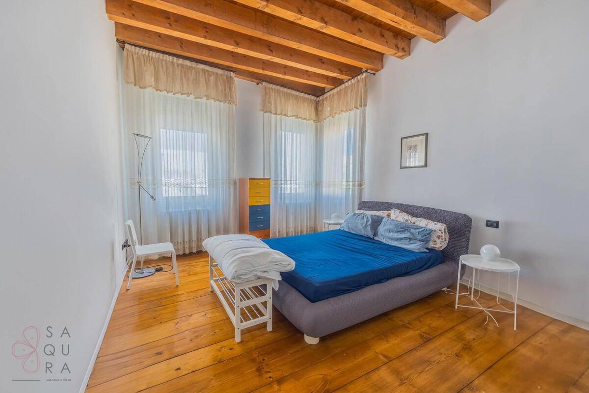Schlafzimmer mit Doppelbett, Dielenboden und rustikaler Holzbalkendecke.