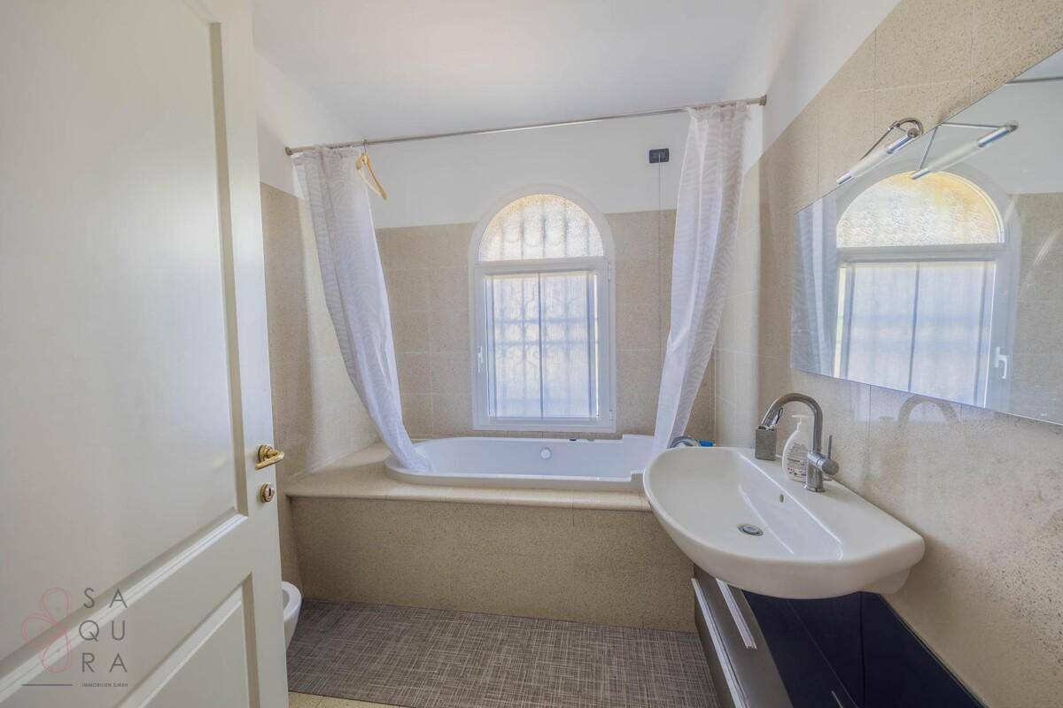Helles Badezimmer mit Badewanne, Fenster und Waschbecken mit Unterschrank.