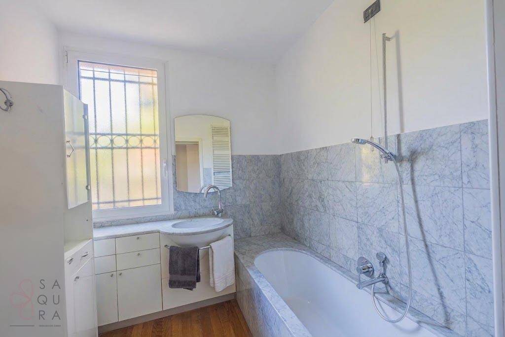 Badezimmer mit Badewanne, Marmorfliesen und Fenster, das viel Tageslicht hereinlässt.