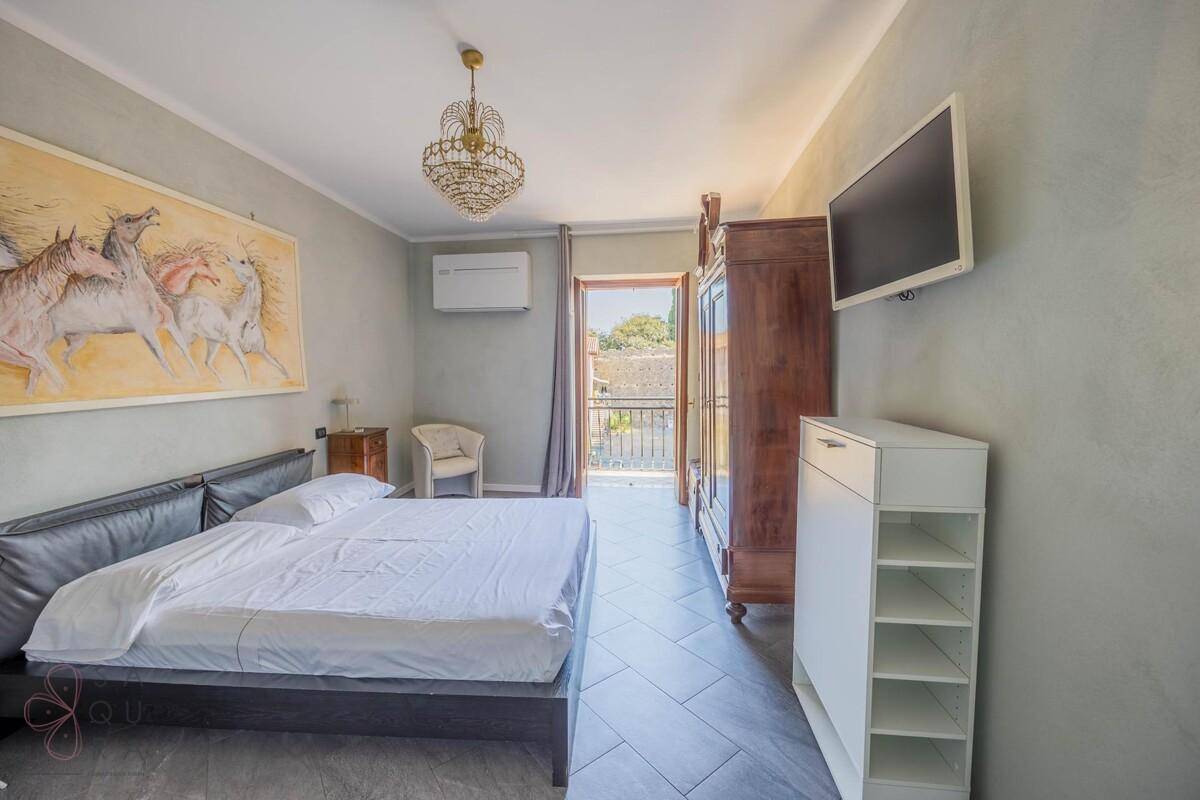 Schlafzimmer mit Holzkleiderschrank, Wandfernseher und Zugang zu einem kleinen Balkon.