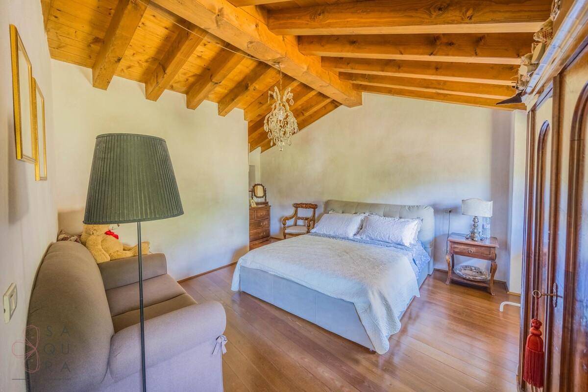 Helles Schlafzimmer mit Holzbalkendecke, Holzboden und gemütlichem Sofa.