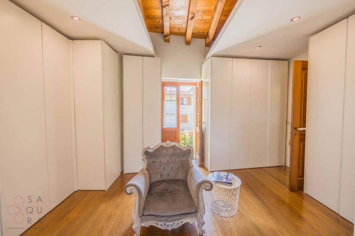 Schlafzimmer mit Einbauschränken, Holzbalkendecke und rustikalem Sessel.