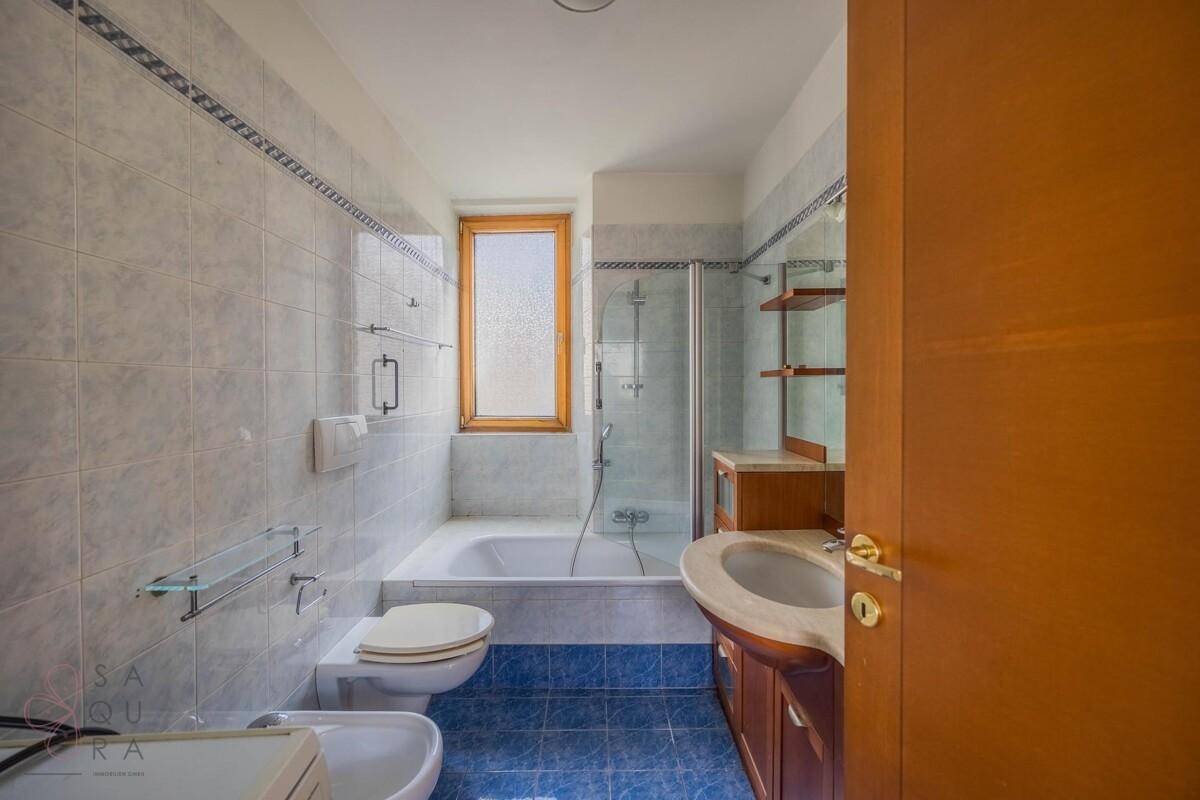 Badezimmer mit Badewanne, Dusche, Bidet, Fenster und blauen Fliesen.