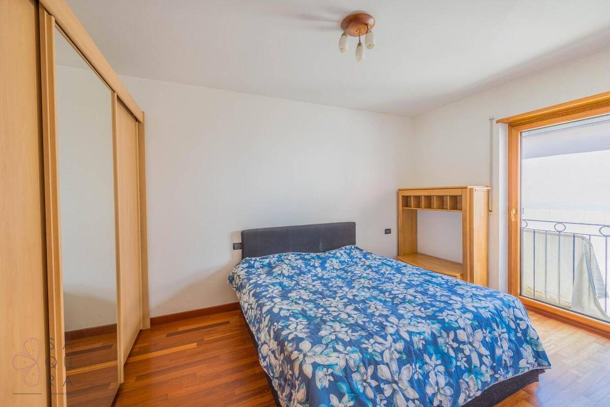 Schlafzimmer mit Doppelbett, Spiegelschrank, Holzboden und Balkonzugang.