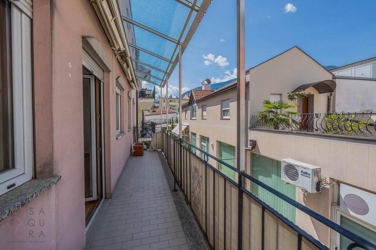Langer, überdachter Balkon mit Fliesenboden und Blick auf die umliegenden Gebäude.