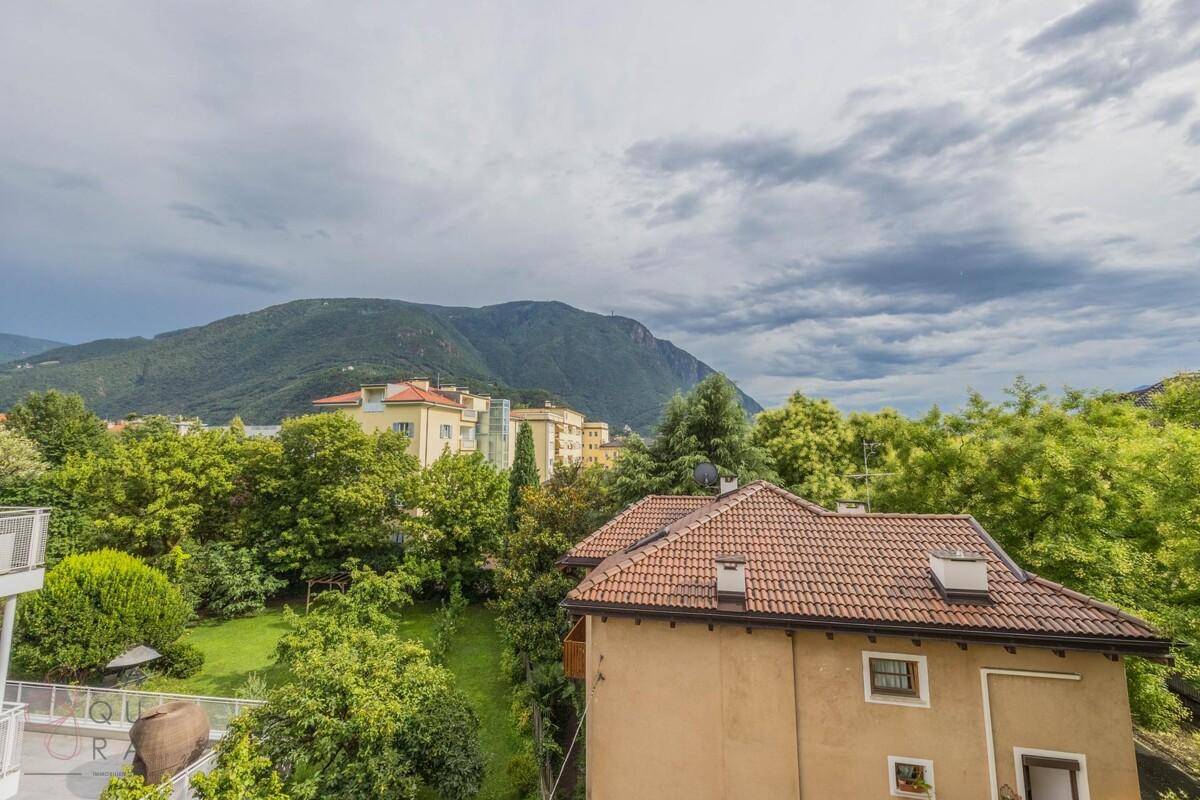 Panoramablick auf grüne Hügel und Berge von einem Balkon, mit traditionellen Dächern im Vordergrund.
